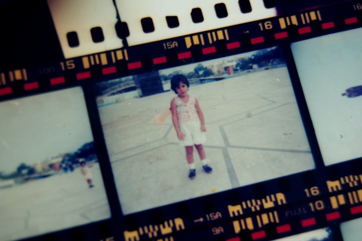 Close-up of a vintage 35mm film strip featuring childhood photos of Daniela Guerrero in Venezuela. High-end film wedding photography roots and heritage. Authentic Fuji film negatives showing the artist's lifelong journey with photography.