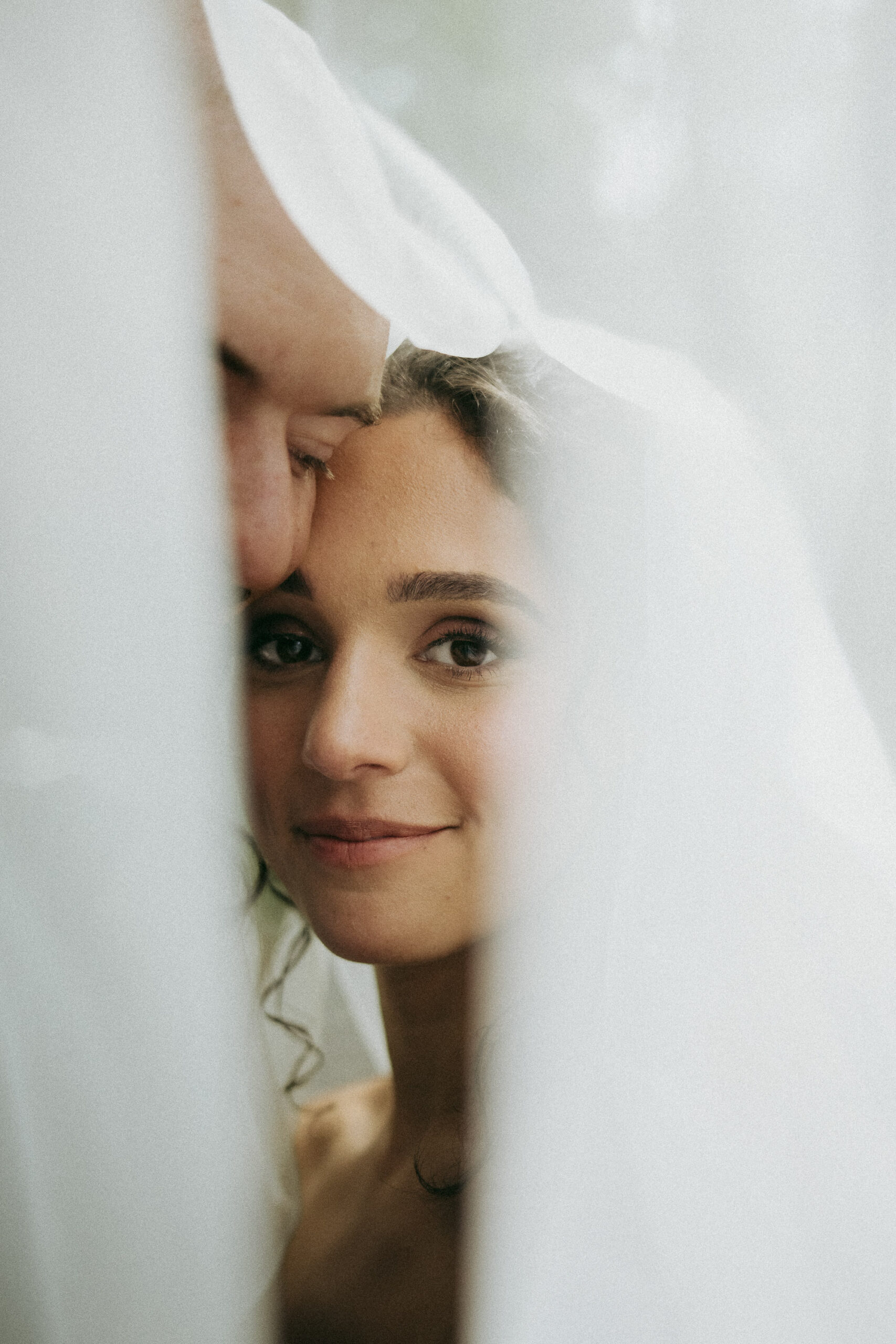 A poetic Biltmore wedding moment by Asheville wedding photographer Daniela Guerrero. A bride and groom share a high-key embrace beneath a sheer veil, symbolizing the mission of preserving fleeting instants through fine art film photography. Biltmore wedding photographer