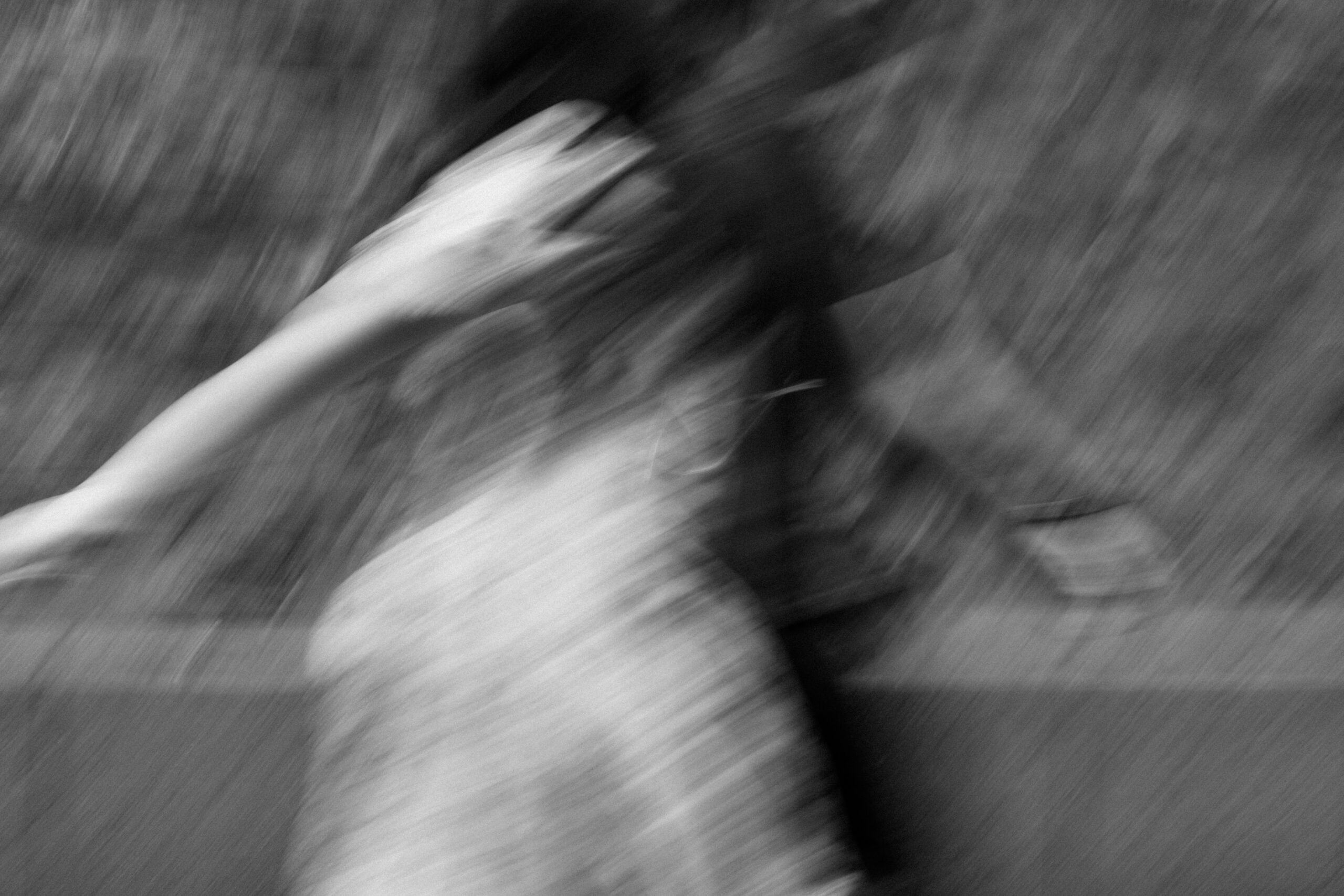 A black-and-white blurry photo shows a person in motion, wearing a light-colored dress with an arm outstretched. The background is indistinct, giving a sense of movement and abstraction. Asheville wedding photographer