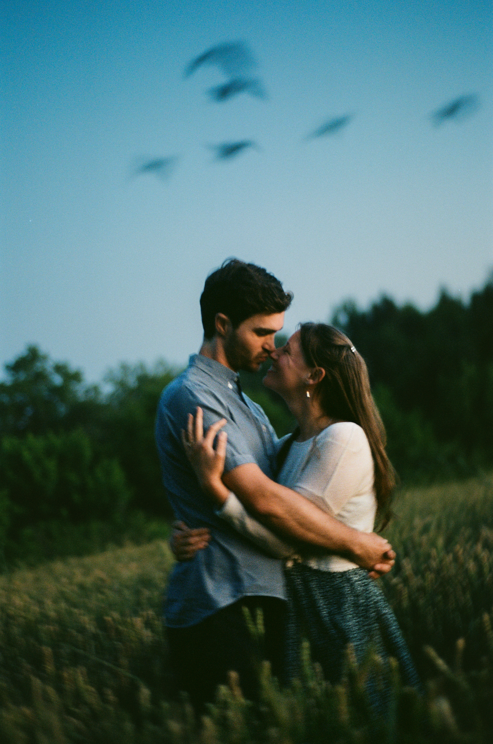 Engagements Portfolio Preview, Couple embracing at sunset with birds in sky, engagement session captured in film